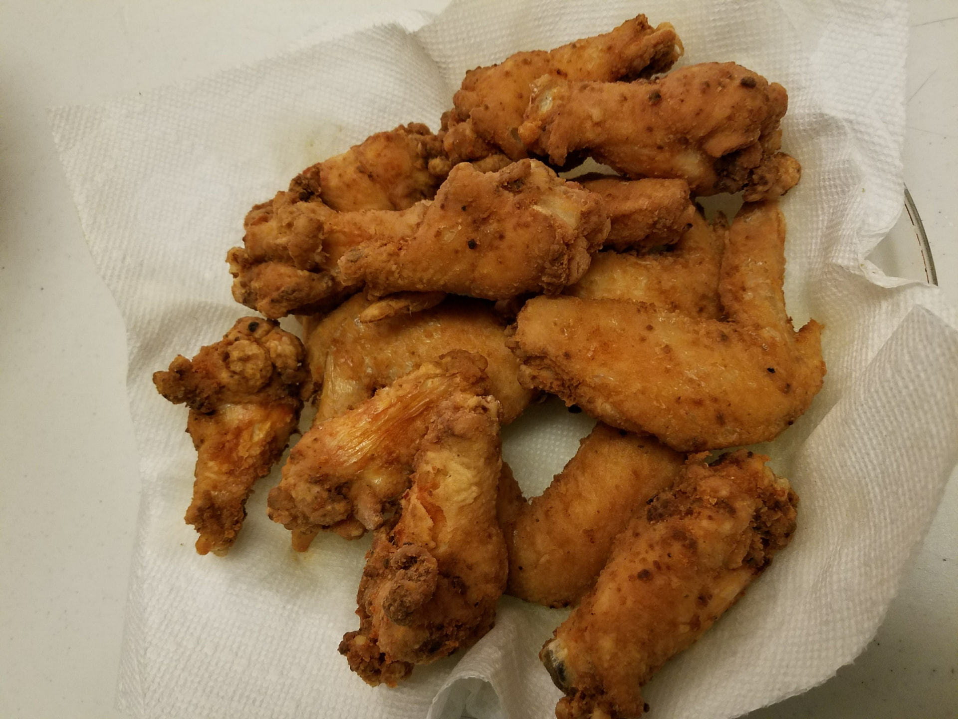 Golden-brown crispy fried chicken wings piled on a paper towel-lined plate to drain
