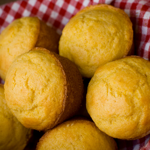 Freshly baked golden cornbread muffins resting in a basket lined with a red-and-white checkered cloth